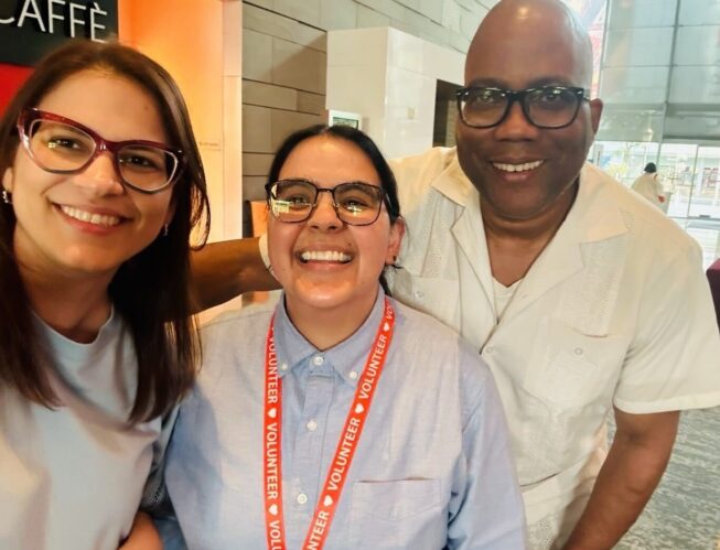 Geo at the HIP conference wearing a lanyard and smiling with two other attendees.